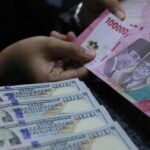 Close-up of hands counting US $100 bills and Indonesian 100,000 rupiah notes.
