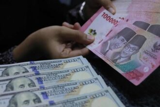 Close-up of hands counting US $100 bills and Indonesian 100,000 rupiah notes.