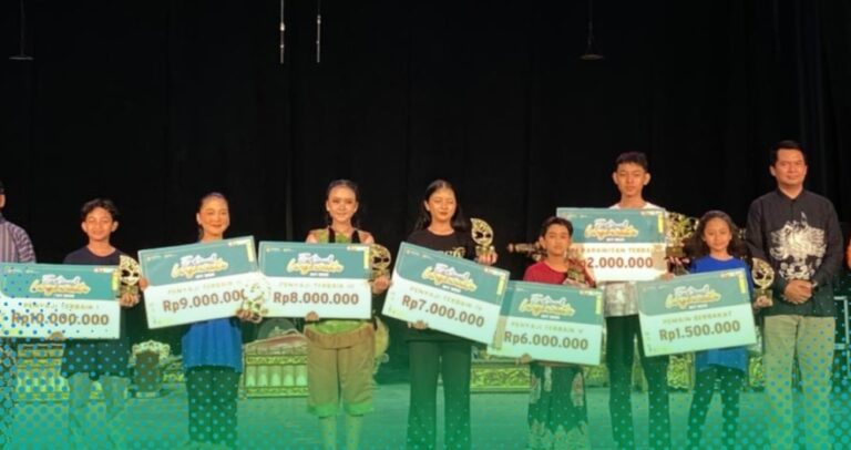 Group of children on a stage holding oversized ceremonial checks and trophies after a competition awards ceremony.