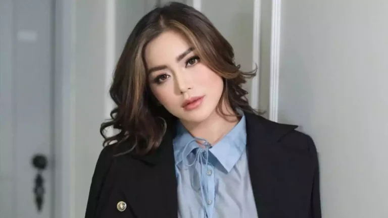 Portrait of a woman with shoulder-length wavy hair, wearing a light blue blouse and black blazer in an indoor setting.