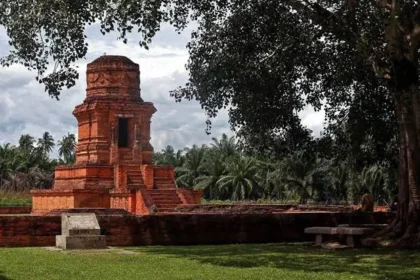 Red brick ancient tower ruin on a raised platform in a palm-lined courtyard garden